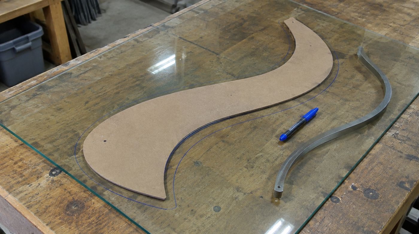 A hardboard template of an irregular curved shape laid on a sheet of glass